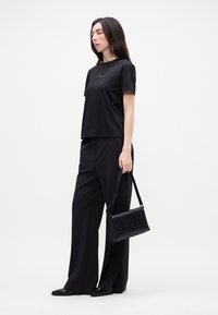 Čierne bavlnené tričko s vyšitým zlatým textom, skombinované s čiernymi pruhovanými nohavicami a čiernou koženou crossbody taškou. Oblečenie dopĺňajú ploché topánky.