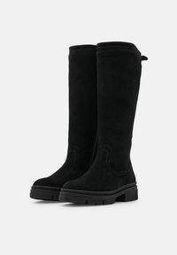 Botas de ante negras hasta la rodilla con suela de goma plana, sutil detalle de costura y cierre de cremallera en el lateral para facilitar su uso.
