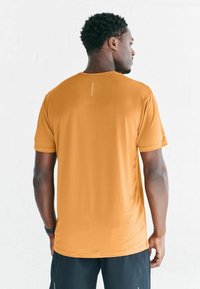 Pomarańczowa sportowa koszulka z krótkim rękawem wykonana z oddychającego materiału; posiada subtelny wzór z odblaskowym akcentem na plecach.