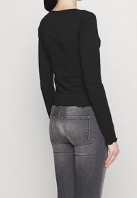 Mustat pitkät hihattomat paidat, jotka on valmistettu puuvillasta, vartalonmyötäinen malli, jossa on aaltoileva helma, yhdistettynä harmaisiin skinny-farkkuihin, joissa on taskut.