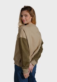 Felpa beige e verde oliva con maniche lunghe e polsini a costine. Realizzata in tessuto morbido, con una vestibilità rilassata e scollatura rotonda.