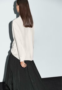 Blusa bianca in satin a maniche lunghe con una vestibilità ampia, abbinata a una gonna nera plissè. Il tessuto testurizzato aggiunge interesse visivo.