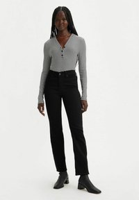 Jeans negros de alta cintura combinados con una blusa de manga larga a rayas en blanco y negro con un escote abotonado y corte ajustado.