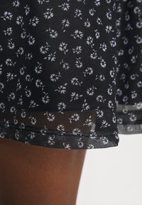 Schwarzer Rock mit floralen Mustern in Weiß, aus leichtem Material, mit transparenter Säume und subtiler Textur.