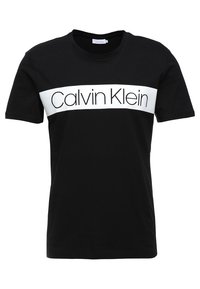 Camiseta de algodón negra con cuello redondo, que presenta una banda horizontal blanca mostrando "Calvin Klein" en letras negras.