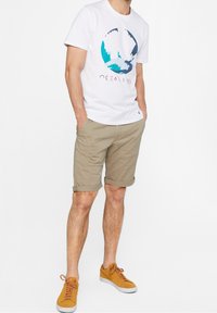 White cotton t-shirt with a colorful circular ocean graphic, paired with beige shorts, and orange sneakers with white soles.