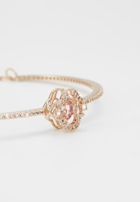 Bracciale in oro rosa con un design floreale, caratterizzato da una pietra centrale rosa e cristalli trasparenti circostanti, che mette in mostra un'arte metallica intricata e una finitura liscia.