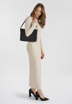 Bolso negro de hombro hecho de material suave, con una sola correa y herrajes plateados, combinado con un vestido de punto beige ajustado y tacones negros.