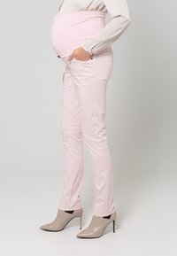 Jeans da maternità rosa chiaro con vita regolabile, vestibilità slim e tasche laterali, abbinati a scarpe con tacco beige.
