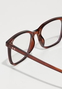Ochelari de vedere tortoise brown cu un cadru rectangular, lentile transparente și o finisare netedă și lucioasă. Accentele includ mici cuie metalice pe brățări.