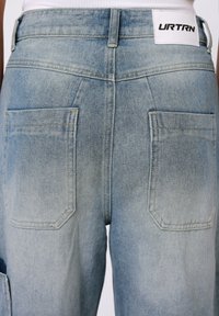Lys blå denim cargo-bukser har en lett falmet finish, to store baklommer og et merke med "URTRN" på livet.