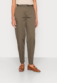 Olivgröna, tapered byxor med slim fit, som har en platt front, bältesöggor och ett matchande skärp. Bruna loafers med gulddetaljer.