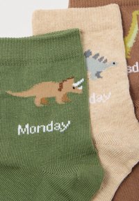 Τρία ζευγάρια παιδικών καλτσών σε πράσινο, μπεζ και καφέ χρώμα. Κάθε κάλτσα διαθέτει γραφικό δεινοσαύρου και την ημέρα της εβδομάδας σε λευκό κείμενο.