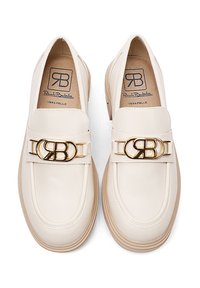 Mocassini in pelle color crema con fibbia logo dorata e suola in gomma neutra. Texture liscia con design minimalista.