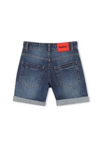Shorts en denim avec un ourlet retroussé, un lavage bleu foncé et une étiquette rouge à l'arrière portant le nom "HUGO" écrit en noir. Deux poches arrière sont visibles.
