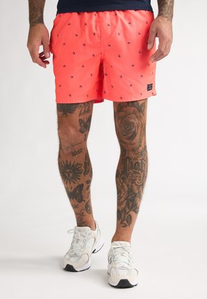 Shorts de bain corail en tissu léger, avec un motif contrasté de petits oiseaux bleu foncé, et une taille élastique.