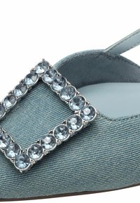 Scarpa slingback in denim blu chiaro con una grande fibbia in cristallo trasparente. Presenta una soletta liscia e una tomaia in tessuto testurizzato.