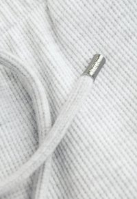 Gray textured fabric with thin diagonal stripes. A gray drawstring with a silver metal aglet featuring engraved text is visible.
