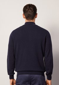 Pull en laine bleu marine avec un col montant, des manches longues et des poignets et ourlet côtelés. Texture lisse sans motifs ni embellissements visibles.