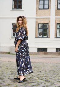Vestido largo y fluido con un patrón abstracto en espiral en azul, negro y crema. Tela suave y ligera con cintura ajustada y mangas cortas.