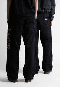 Pantalones negros de corte relajado con un diseño gráfico en rojo en una pierna y un bolsillo trasero, fabricados con una tela suave y duradera.