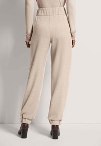 Beige, relaxte broek met een elastische tailleband en gathered cuffs. Gladde textuur, gecombineerd met donkere enkellaarsjes met hak.