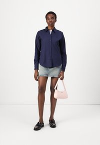 Camicia blu marina con bottoni, gonna mini in denim, mocassini neri e una borsa a spalla rosa con una texture liscia e un branding sottile.