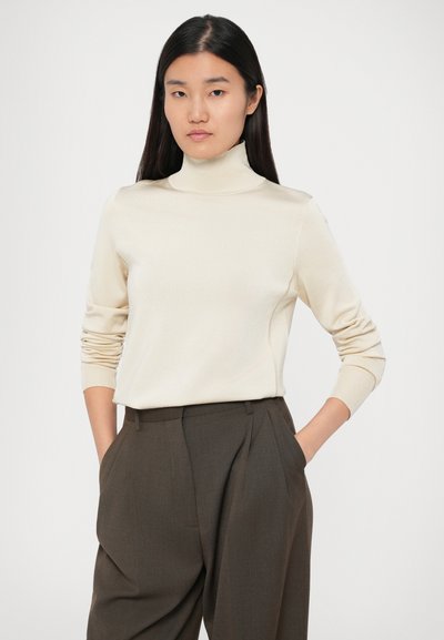 Kafijas krāsas turtlenecks džemperis, izgatavots no gludas auduma, ar pieguļošām piedurknēm, apvienots ar tumši brūnām augsto jostasvietu biksēm ar sānu kabatām.