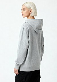 Felpa grigia con una vestibilità comoda, dotata di cappuccio con lacci, polsini a coste e una texture morbida. Indossata con pantaloni cargo neri.