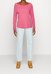 Pink long-sleeve t-shirt with a wide neckline, paired with light blue straight-leg jeans and brown heeled ankle boots. Minimalist design.