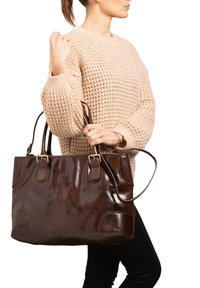 Sac fourre-tout en cuir marron avec une finition brillante, poignées doubles et bords arrondis, présentant des accessoires en métal doré et des accents de couture.