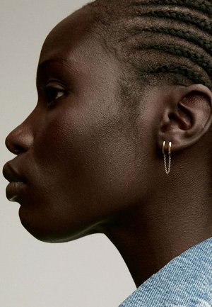 Pendientes de aro de oro con un detalle de cadena de plata colgante, llevados por un modelo con cabello trenzado, mostrando el diseño del pendiente de perfil.