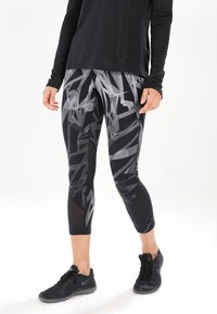 Zwarte sportlegging met een geometrisch grijs patroon, met een aansluitend ontwerp, zijpanelen van mesh en een cropped lengte. Gecombineerd met zwarte schoenen.
