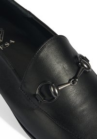 Schwarze Lederloafer mit glatter Textur, runder Form und einem metallischen Akzent mit einem kreisförmigen Link an der Vorderseite.