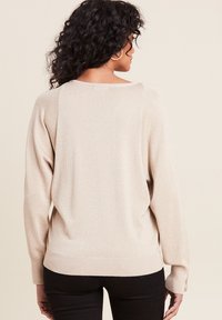 Licht beige, langomgetrokken trui met een zachte textuur en subtiele glans. Heeft een ontspannen pasvorm en ribgebreide manchetten en onderkant.