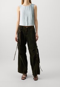 Jasnoniebieski prążkowany crop top w połączeniu z luźnymi, ciemnozielonymi spodniami cargo z wieloma kieszeniami i regulowanymi trokami. Czarne sandały na paski.