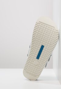 Light blue sneaker with a textured white outsole. Features a blue logo accent and a patterned grip on the sole for traction.