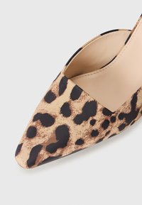 Leopardmønstret stiletto hæl med spids tå og åbnede sider. Stoftekstur med brune og sorte accenter. Glat inderside og sømløs design.