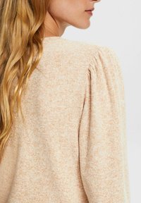Suéter de punto beige claro con tejido texturizado, que presenta hombros abullonados y un escote ligeramente curvado. Acabado suave, color cálido.