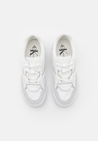Weiße Sneaker mit einem glatten Lederobermaterial, grauen Wildlederelementen, Schnürdesign und einer markierten Innensohle mit "Calvin Klein Jeans."