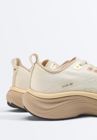 Paire de chaussures de sport beige et crème avec des semelles épaisses et rembourrées, des empeignes texturées et des languettes à l'arrière.