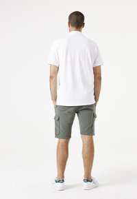 Witte polo, olijfgroene cargoshorts met zijzakken en witte sneakers met groene accenten, gezien van achteren.