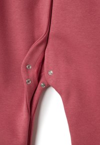 Tutina morbida rosa con chiusure a scatto all'inguine, dal texture liscia e design aderente.