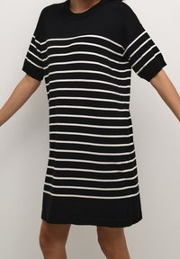 Czarna i biała sukienka koszulowa w paski z krótkimi rękawami, prążkowanym dekoltem, bocznymi rozcięciami i luźnym krojem. Teksturowana dzianina.