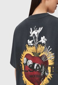Czarna, ciemnoszara, oversize t-shirt z graficznym wzorem przedstawiającym serce z kwiatami i strzałami, zdobionym żółtymi, białymi i czerwonymi akcentami.