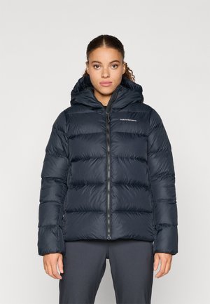 Casaco puffer azul-marinho com capuz, apresentando secções acolchoadas, um fecho éclair à frente e um detalhe de logótipo. Material leve com uma textura suave.