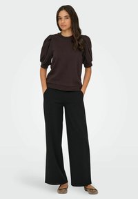 Dark brown pullover with puff sleeves, paired with black wide-leg trousers. Fabric appears soft with a relaxed fit and minimalistic design.