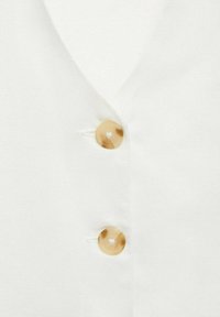 Bijela tkanina s dizajnom u obliku V-izreza, koja ima dva bež, okrugla gumba, s glatkom teksturom i suptilnim sjajem.