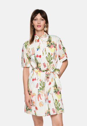 Woman wearing short-sleeve belted dress with colorful cactus, lipstick, hearts, chili peppers, and other playful print patterns on white background.