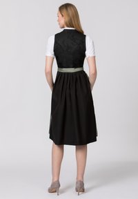 Schwarzes Kleid mit tailliertem Oberteil, grünem Satin-Taillenband und plissiertem Rock. Hat einen strukturierten Rückenteil und weiße, puffärmelige Ärmel. Graue Absätze.